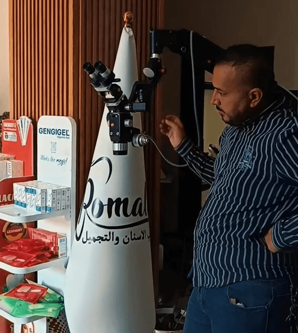 Person inspects Karl Kaps "Microscopes made in Germany" atop cone. Shelf of dental products nearby.